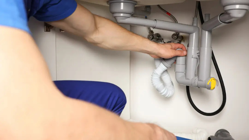 Professional plumber inspecting pipes under a bathroom sink in Oakville Ontario